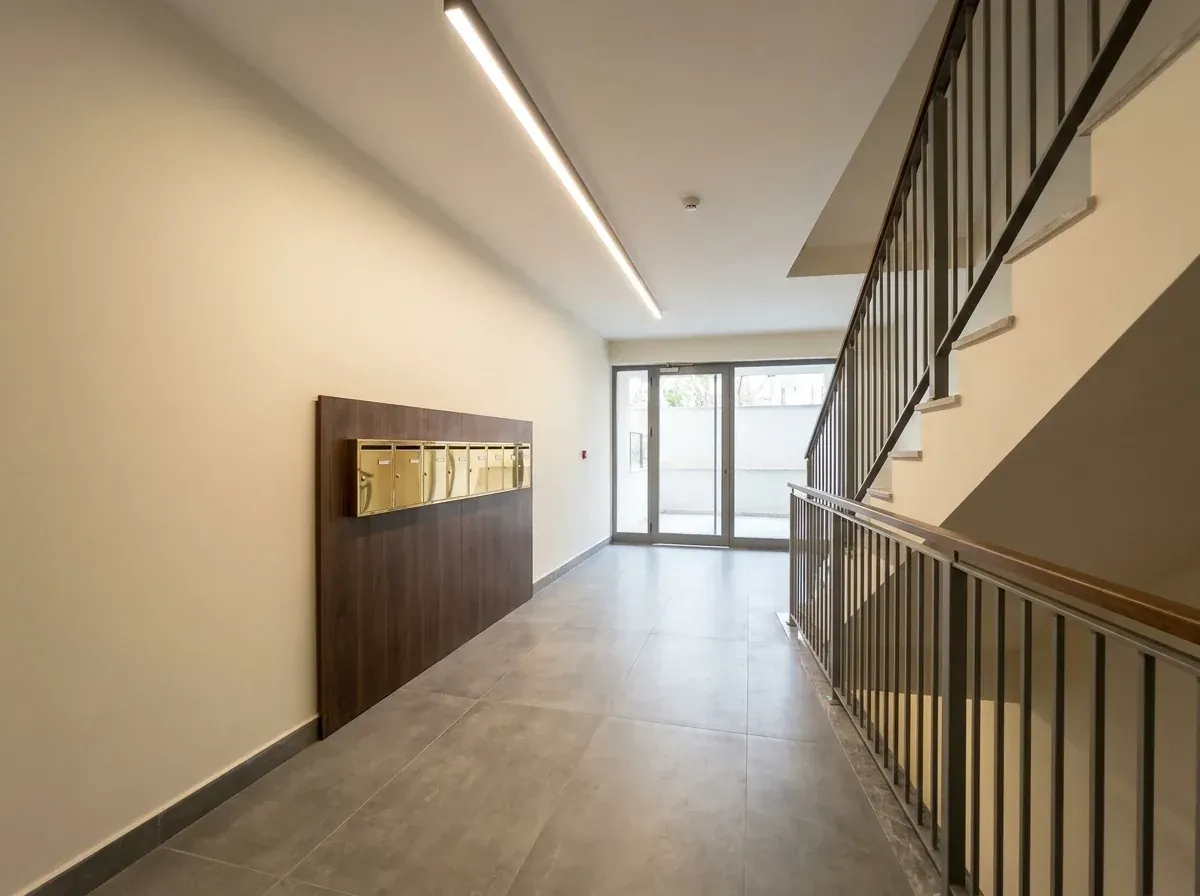 Yenilenmiş apartman girişinde gri porselen zemin, ahşap panel ve çelik korkuluklu merdiven