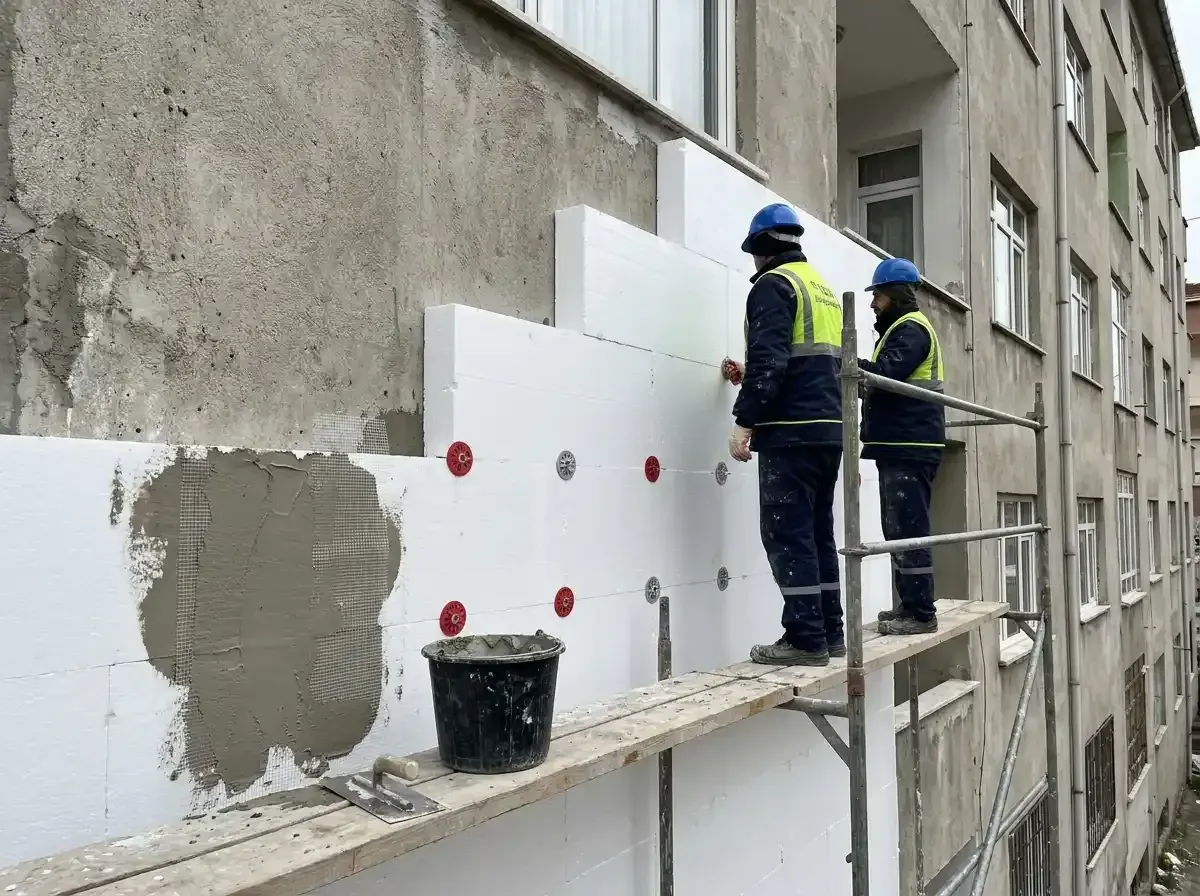 İskelede duran işçiler cepheye beyaz yalıtım levhalarını dübelle sabitliyor